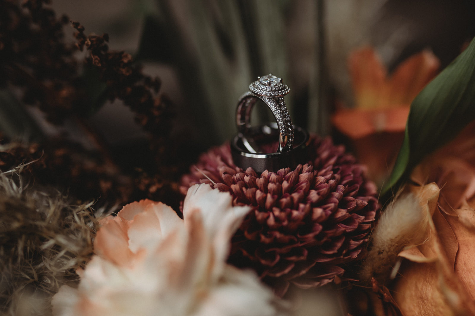 White gold halo engagement ring and men's wedding ring by Marlow Design styled on top of a dried floral bouquet