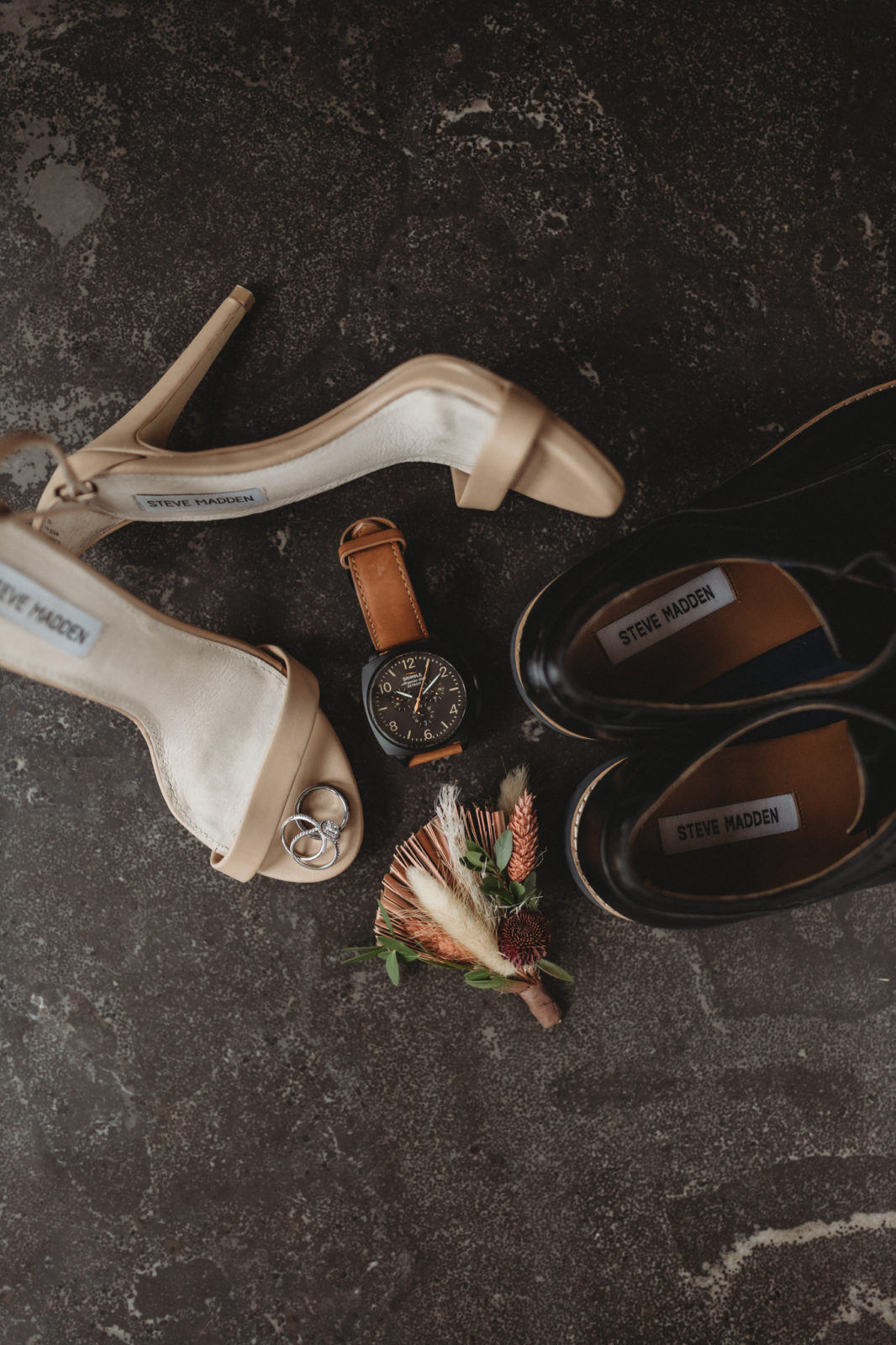 Styled flatlay against a charcoal background featuring gold heel and grooms shoes by Steve Madden