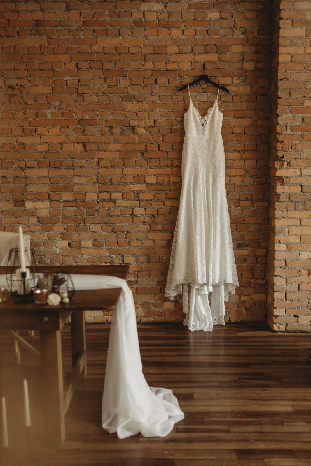 Anais Anette Flagship lace gown hanging on display against a brick wall at The Garret