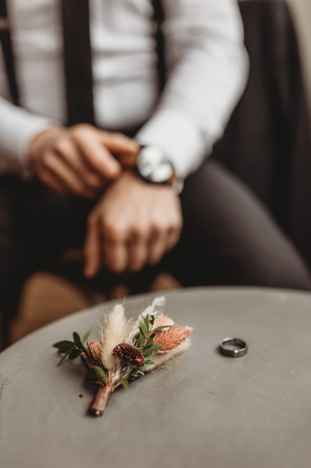 Dried floral boutineer by Stemistry Floral Design Co with the groom fixing his watch in the background