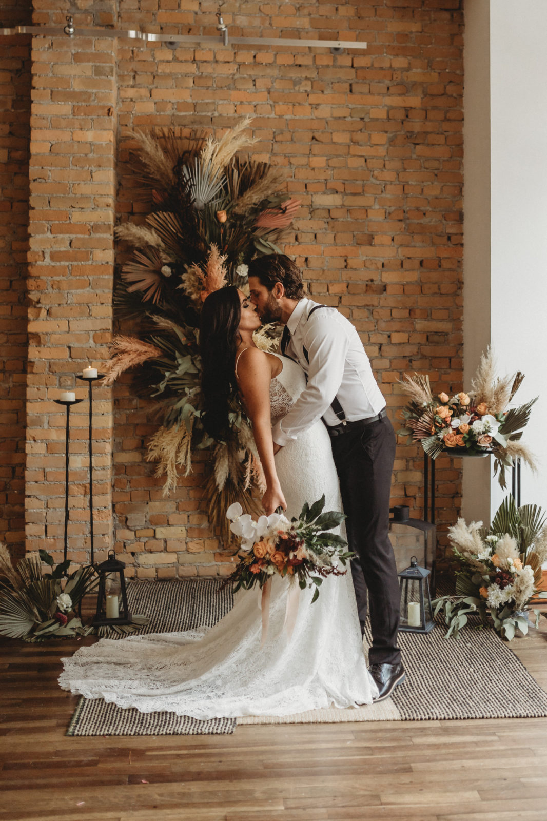 Modern bride and groom kiss in front of a boho dried floral installation for a downtown Calgary wedding at the Garret