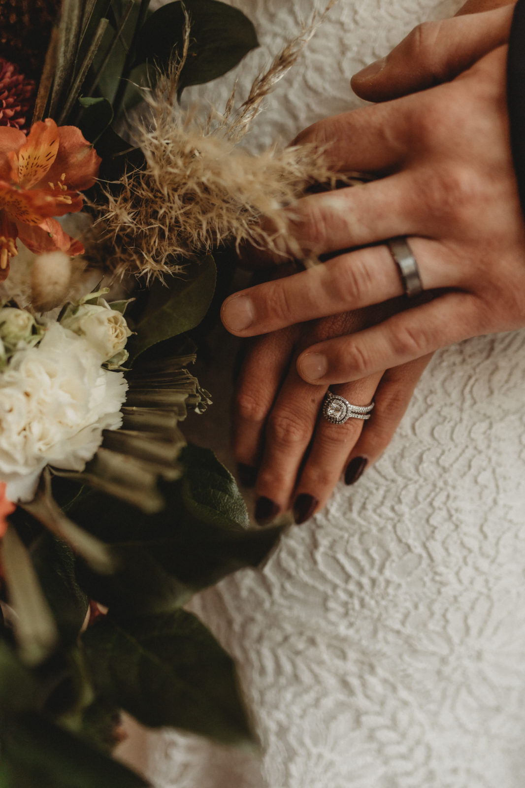 Bride and groom's hand together with a dried floral wedding bouquet in the foreground