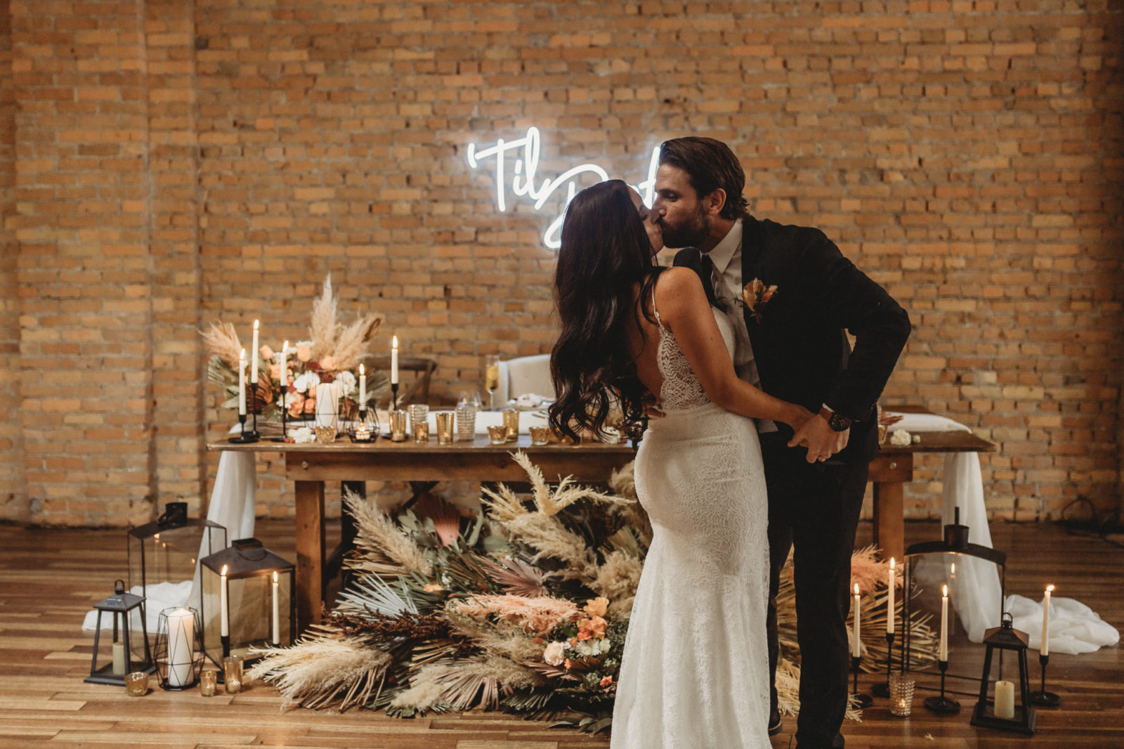 Groom kisses his bride in front of their dried floral styled sweetheart table at The Garret