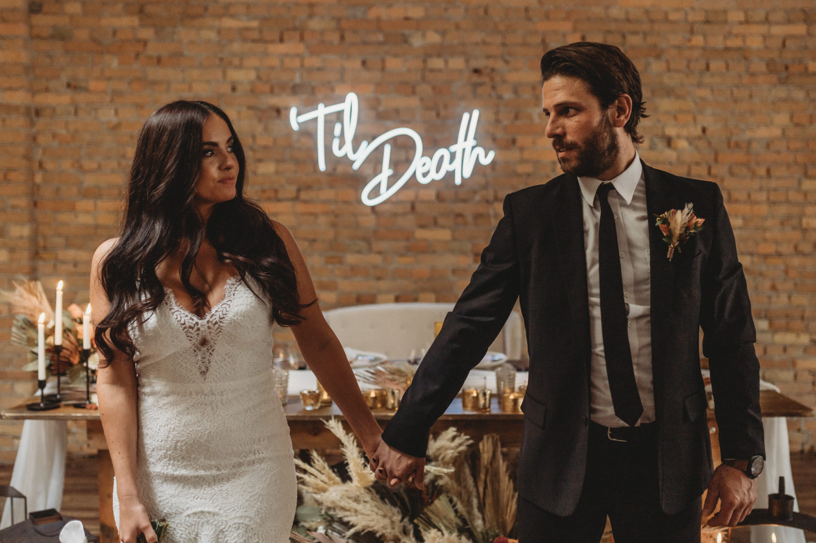 Down to earth bride and groom hold hand in front of a Till Death sign