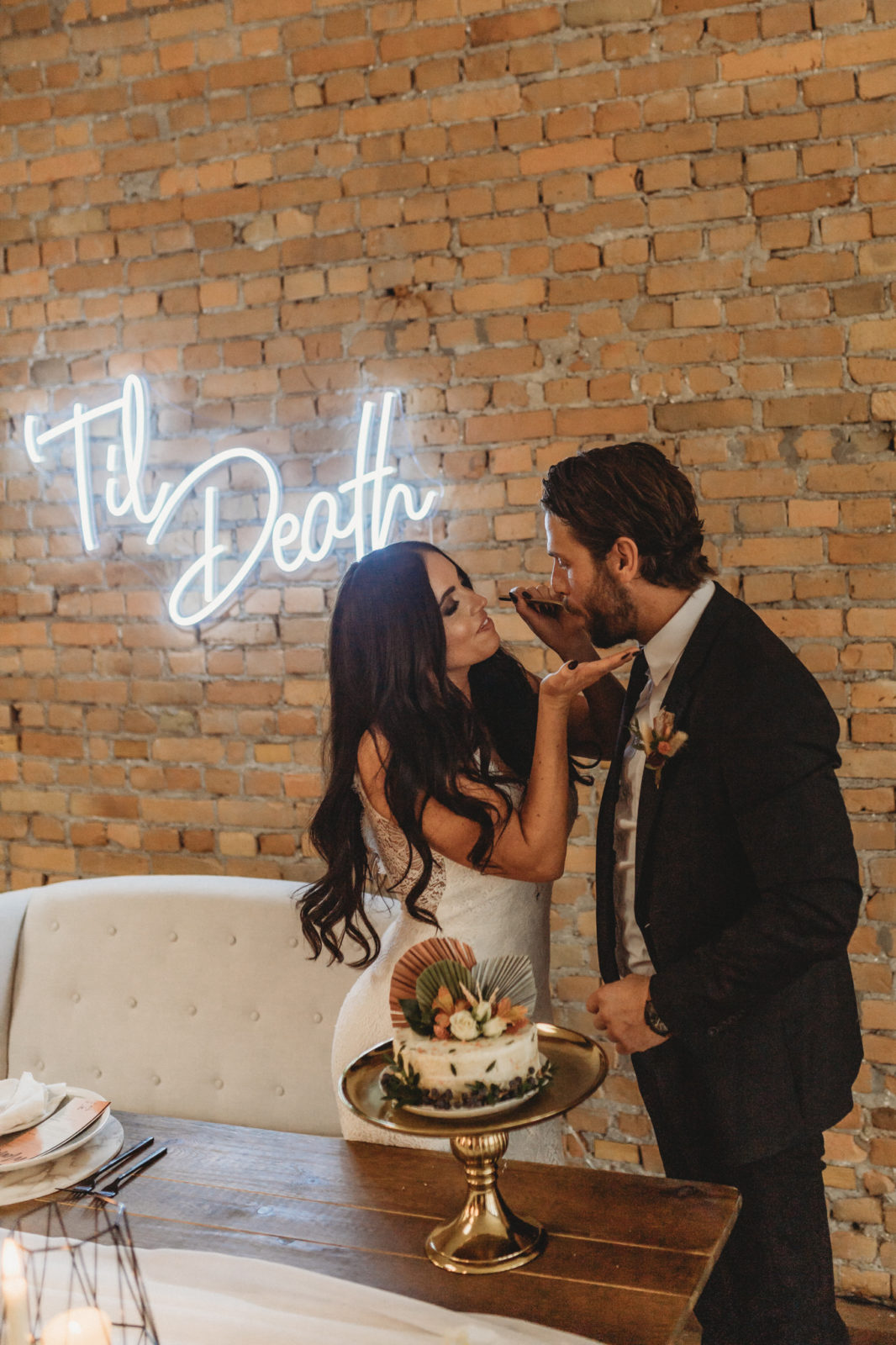 Modern boho bride feeds her groom a piece of wedding cake in front of a Till Death sign