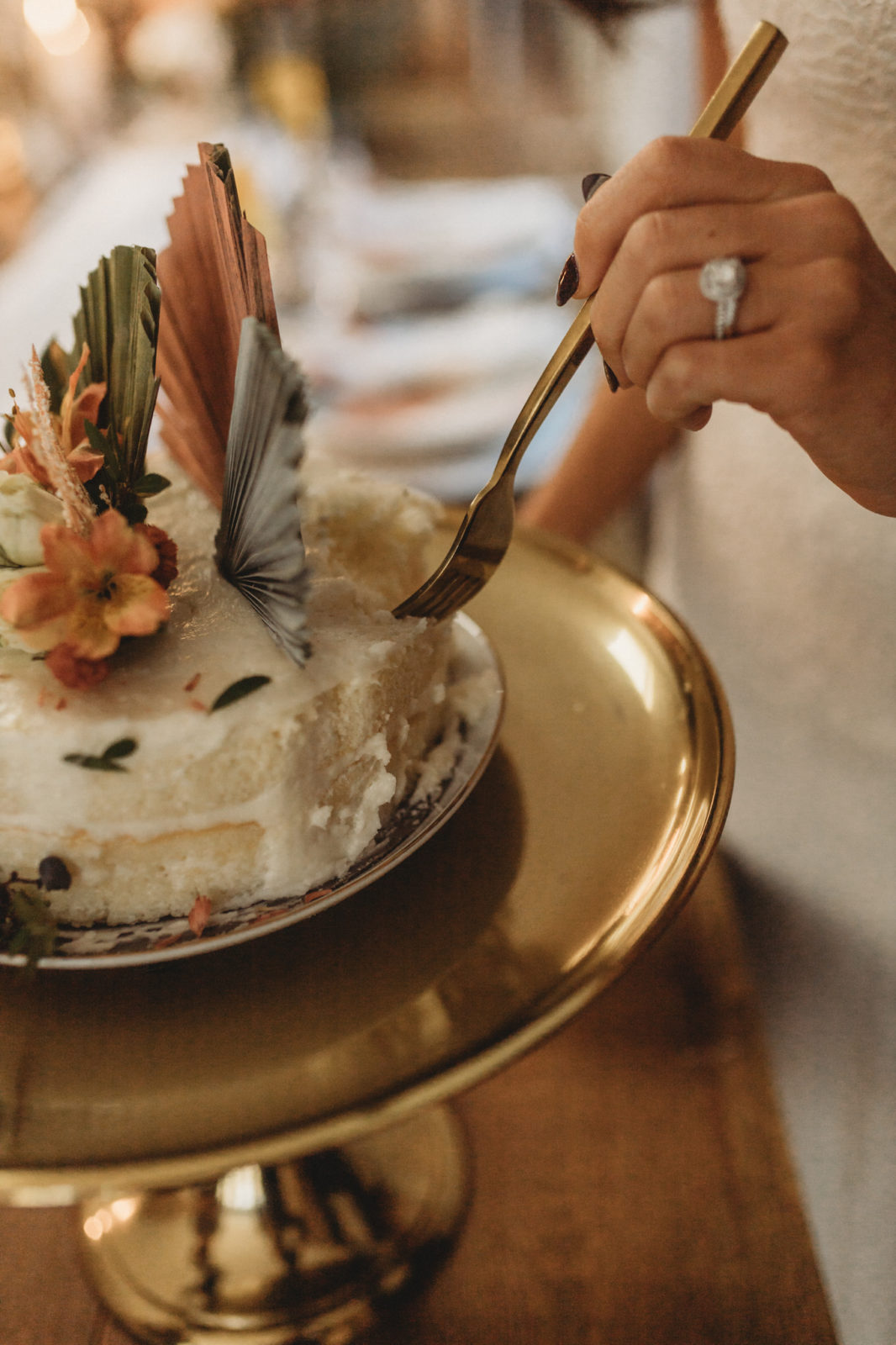 Bride cuts into her white, orange and sage wedding cake 
