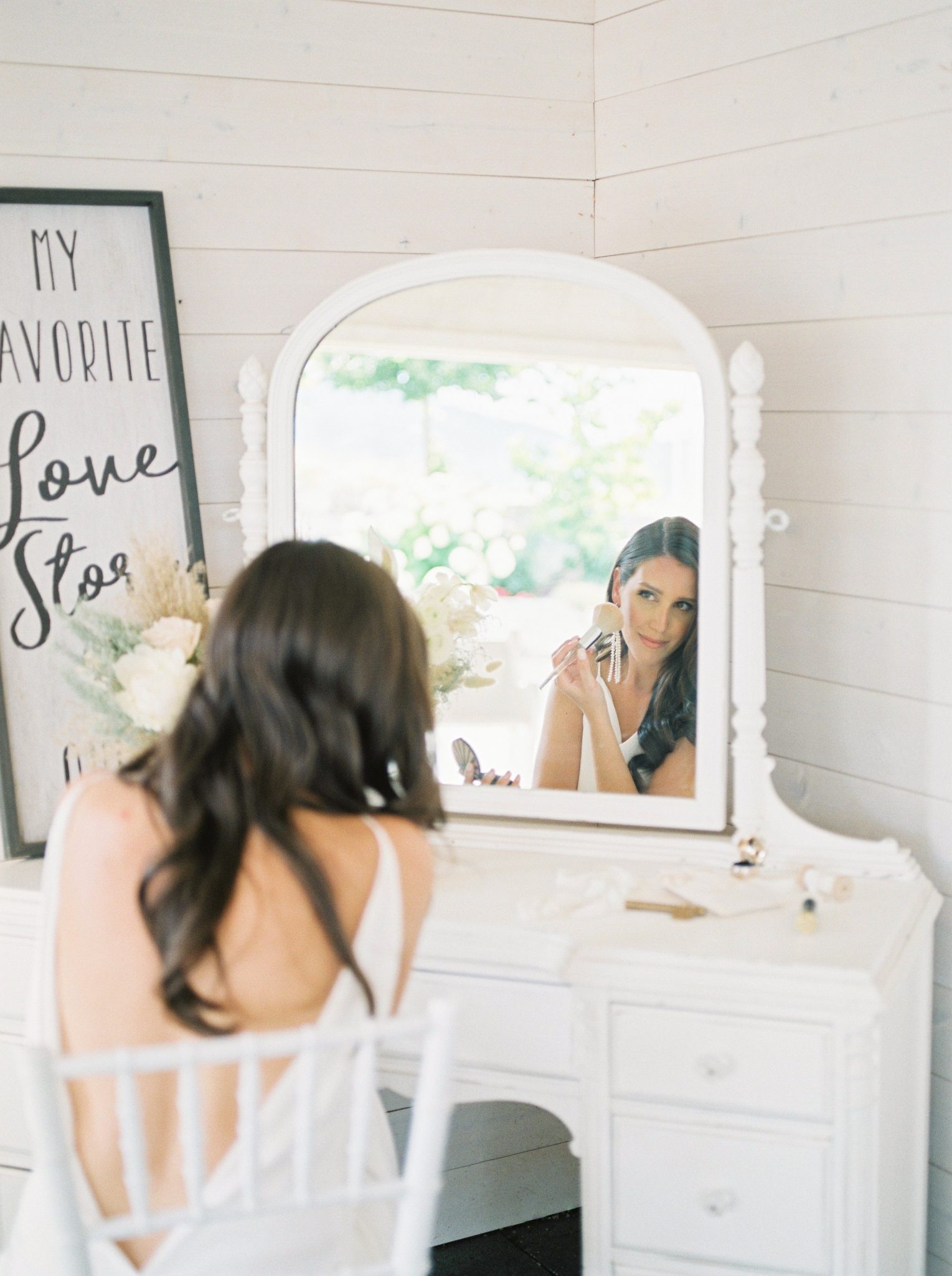 Modern Okanagan bride applies makeup seated in front of a white vanity