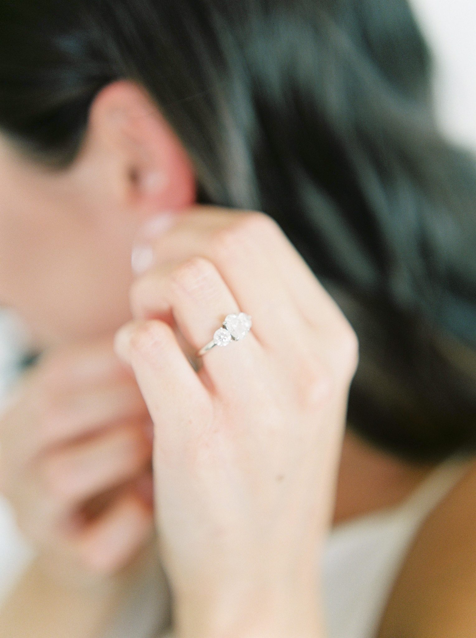 A modern Okanagan bride adjusts her bridal earrings with her engagement ring in the foreground