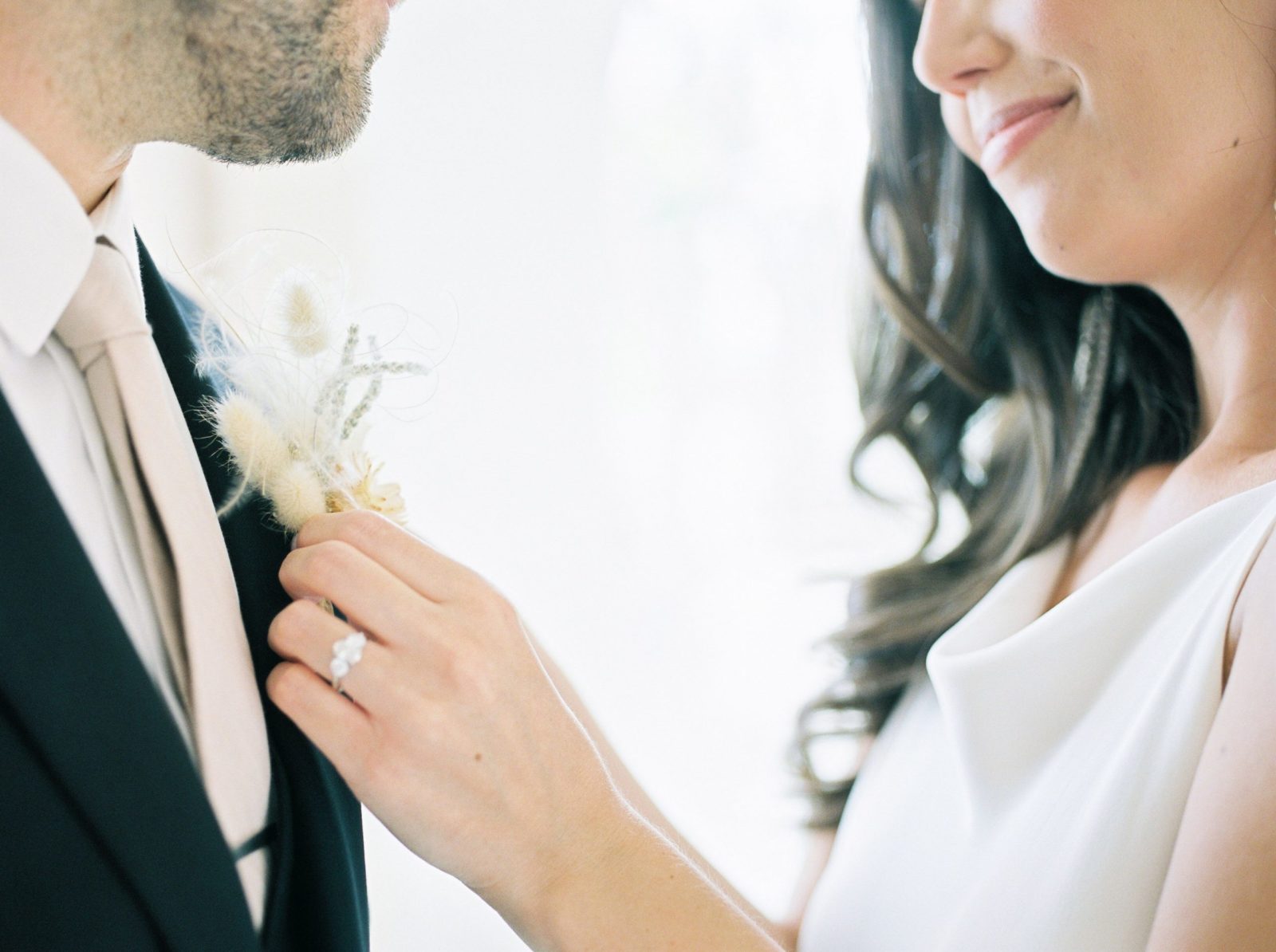 Modern Okanagan bride adjusts her groom's boho boutonnière