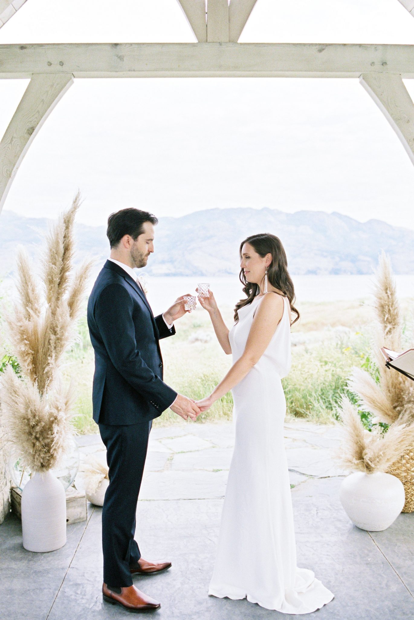 Bride and groom clink glasses surrounded by pampas grass at their modern Okanagan ceremony 