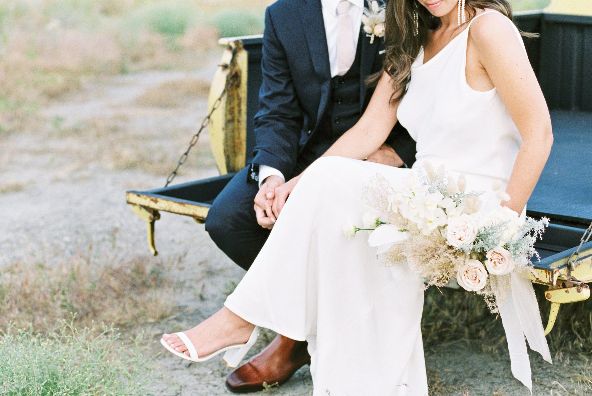 Bride and groom sit on the tailgate of a yellow pickup truck