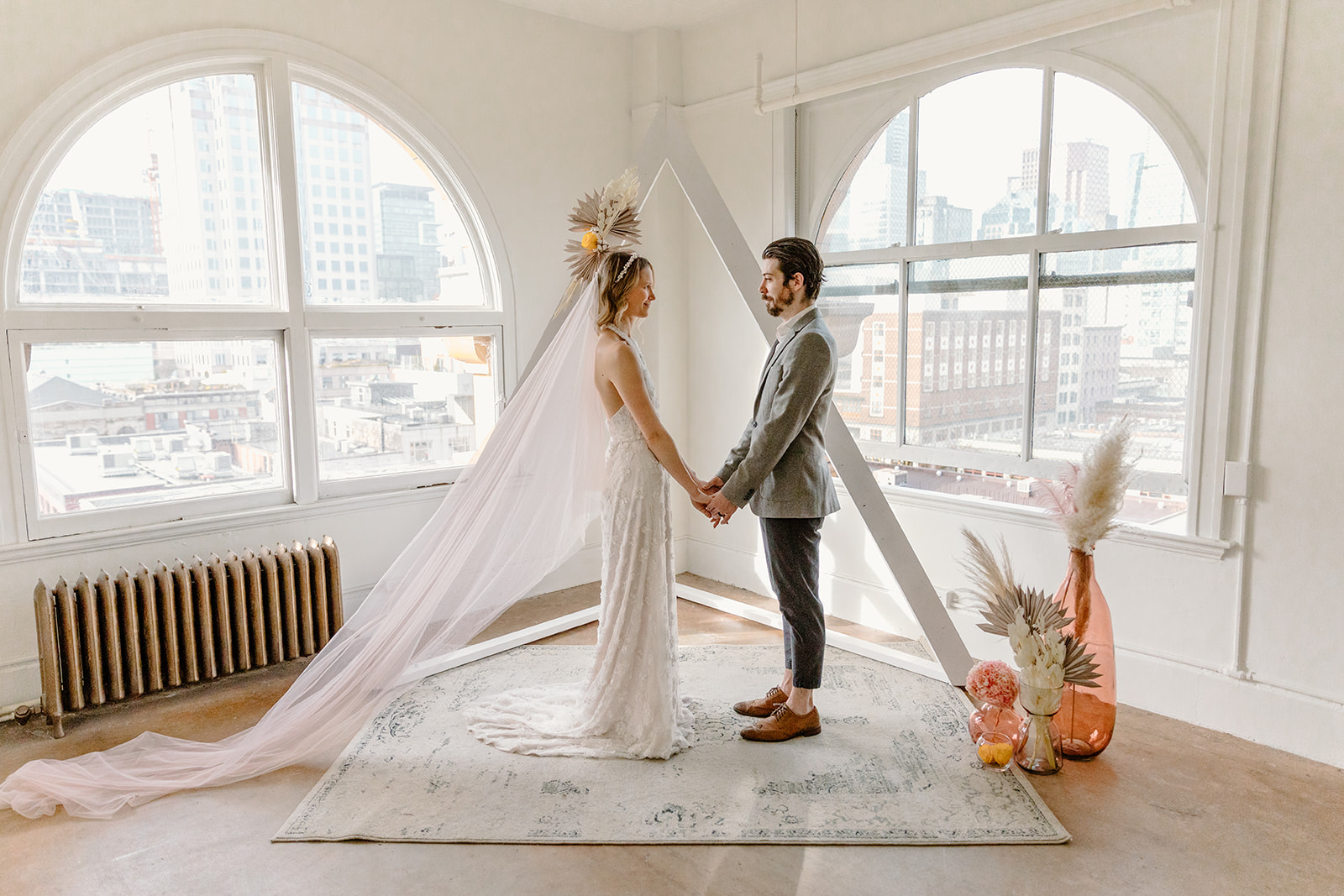 Bride and groom pose in front of modern ceremony decor including a white triangle arch, a rug and dried boho florals