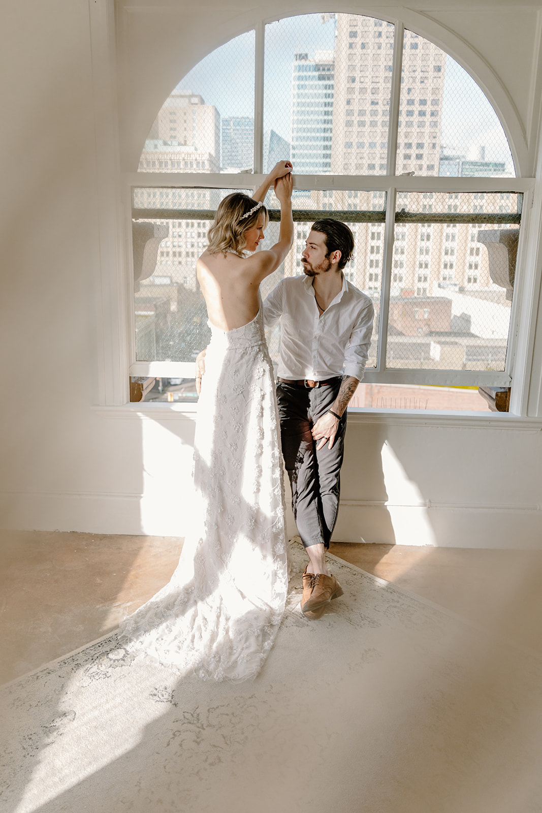 Bride and groom pose in front of a wide arched window in Gastown Vancouver