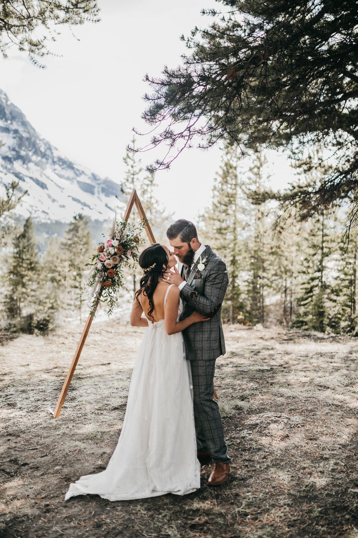 Bride and groom pose in front of a triangle arch in the mountains