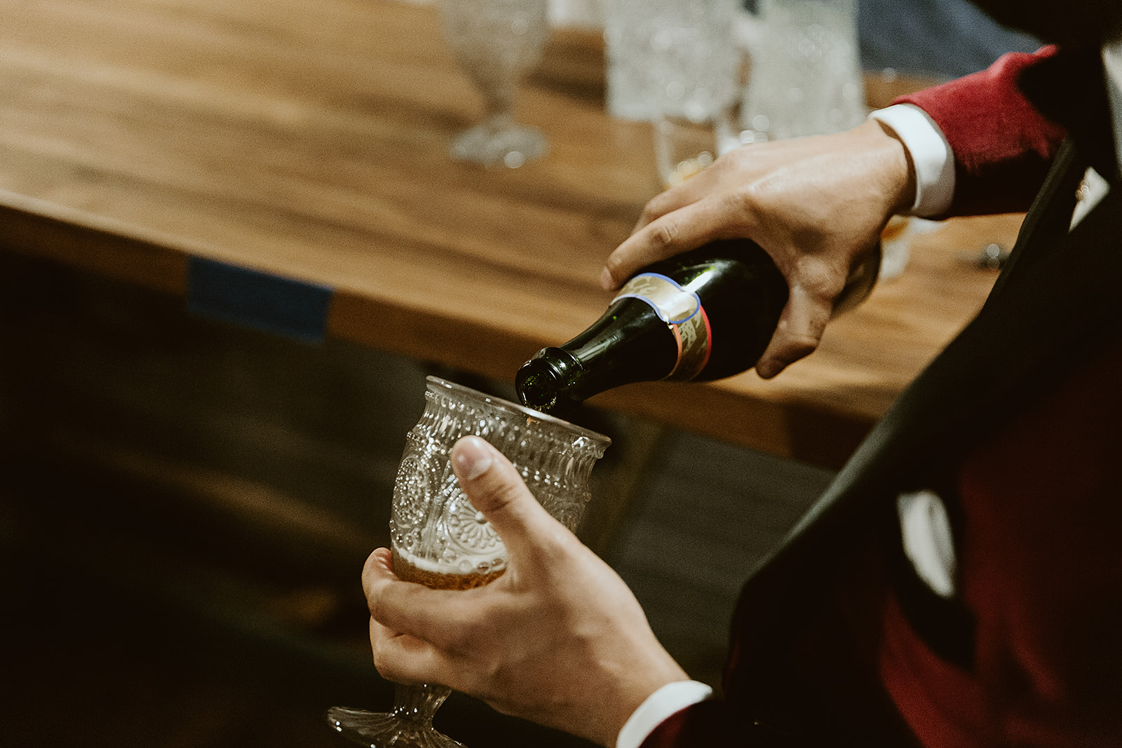 Groom in a crimson suit pours beer into a glass