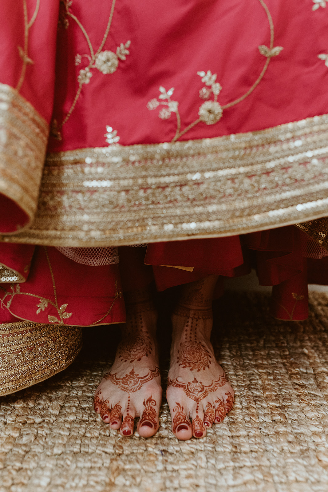 Hena on a bride's feet while she stands in a bright pink lehenga