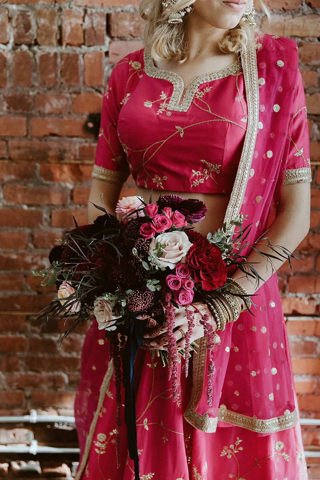 Bride in a bright pink lehenga holds a jewel tone inspired bridal bouquet