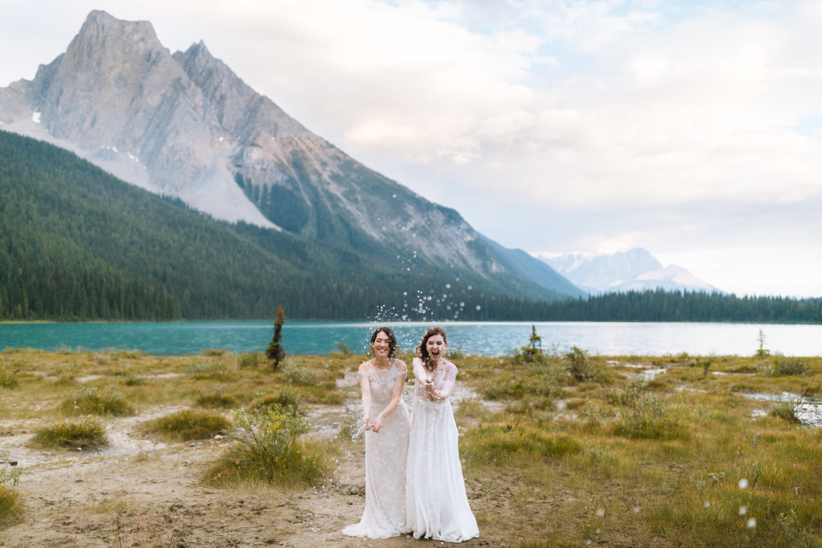 Newly wed couple pops champagne on the shores of Emerald Lake with the mountains of Yoho National Park in the background