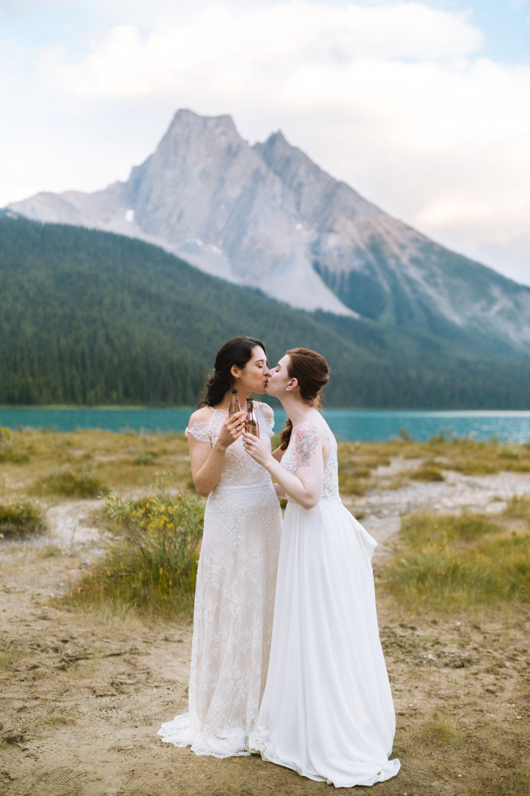 Newly wed couple shares champagne and a kiss on the shores of Emerald Lake with Yoho National Park mountains in the background