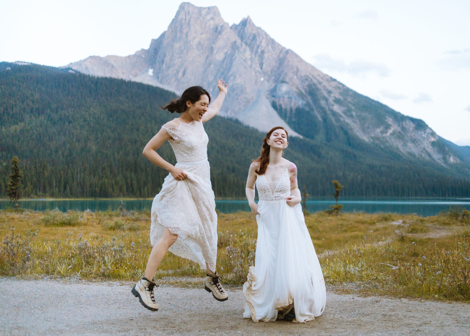Newly wed couple strike a playful pose in their gowns and hiking boots with the mountains of Yoho National Park in the background