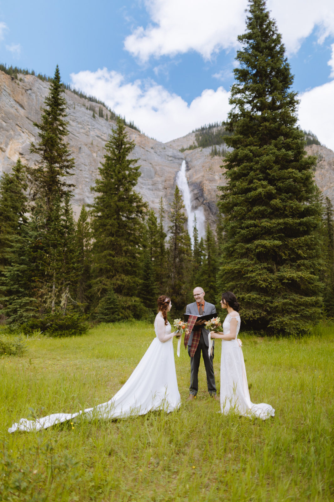 Two brides say their vows in a hand fastening ceremony with Takakkaw Falls in the background for this Yoho National Park Elopement
