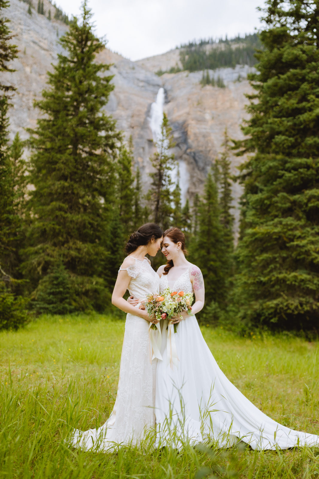 Newly weds pose in their wedding gowns in front of Takakkaw Falls for their Elopement in Yoho National Park