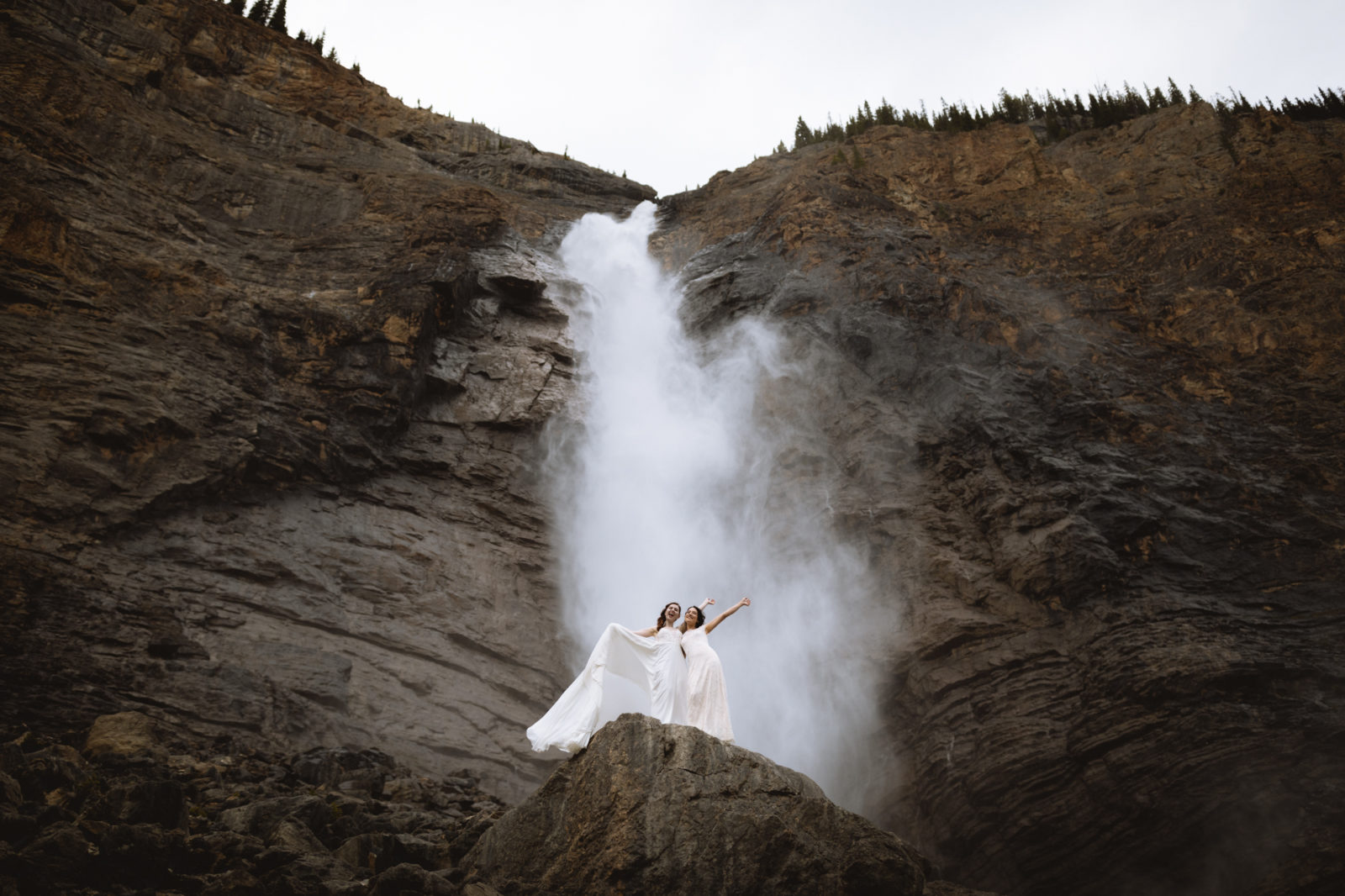 Newly wed brides strike a pose in front of Tawakkawa Falls in Yoho National Park