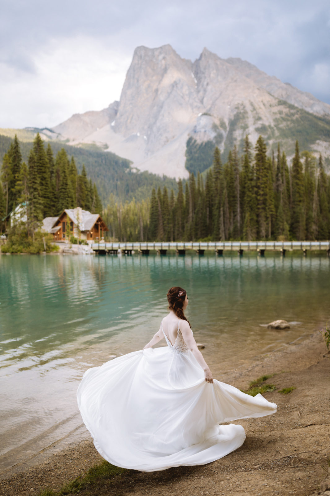 Bride shows off her romantic gown by twirling on the shores of Emerald Lake with Emerald Lake Lodge in the background