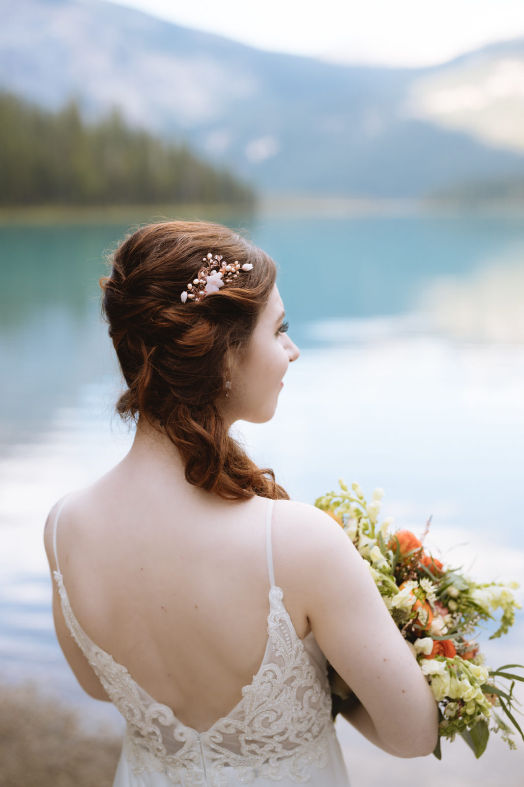 A bride wearing a delicate bridal accessory in her hair stands next to Emerald Lake for her Elopement in Yoho National Park