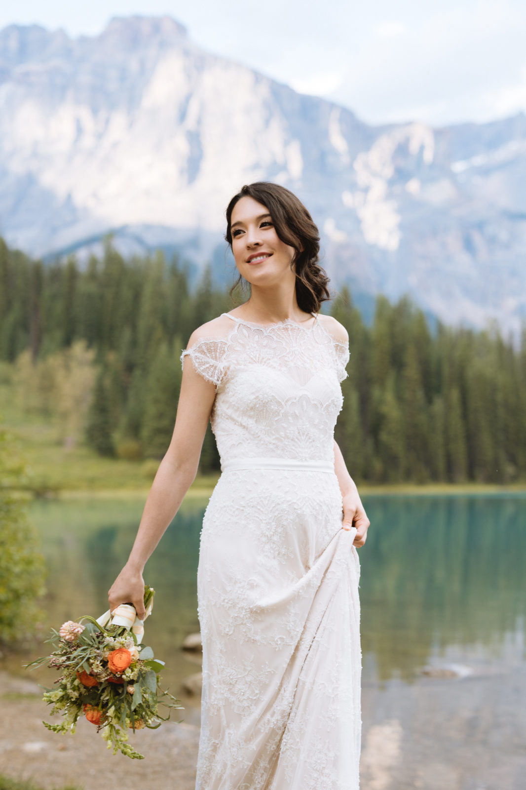 Bride poses next to Emerald Lake with Yoho National Park mountains in the background