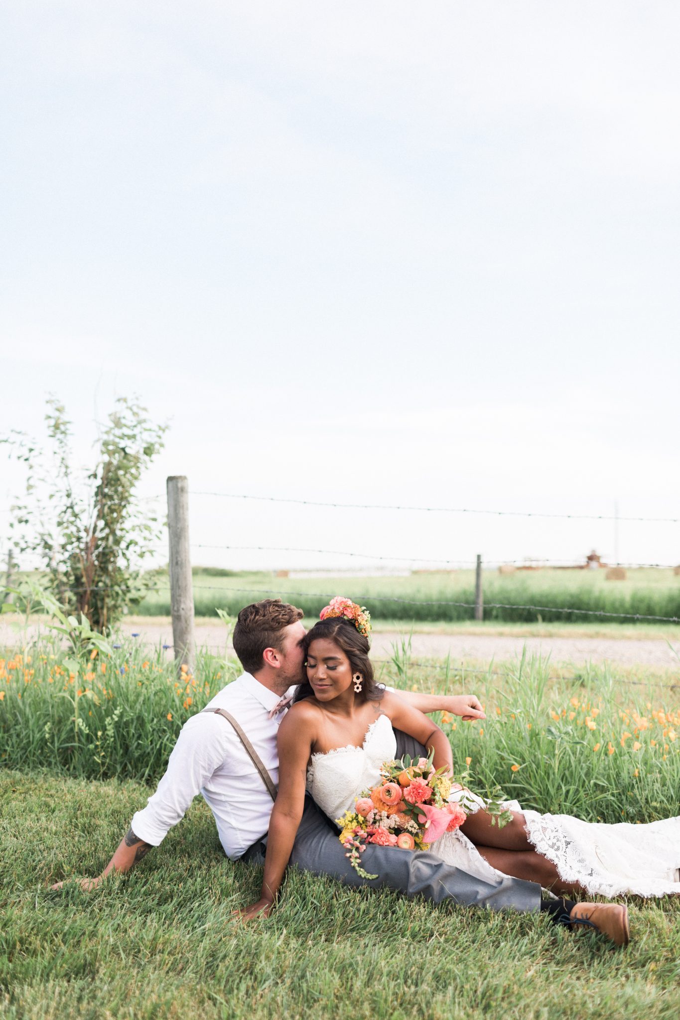 Bride and groom pose in the grass for this countryside southern Alberta wedding with tangerine flowers