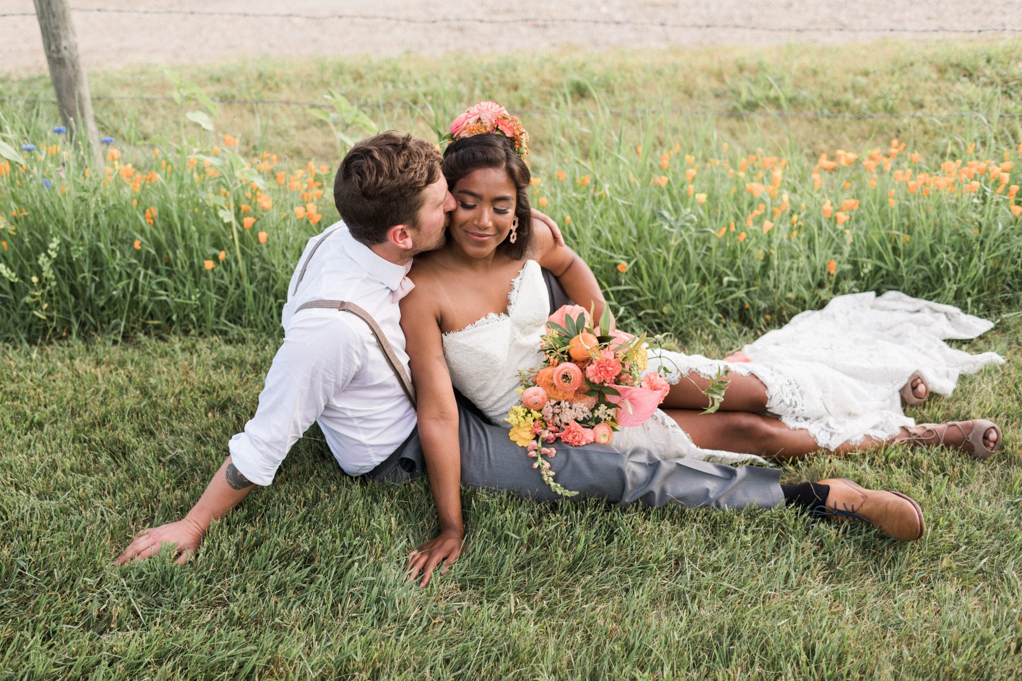 Bride and groom sit together in the grass for this countryside inspired wedding with tangerine flowers