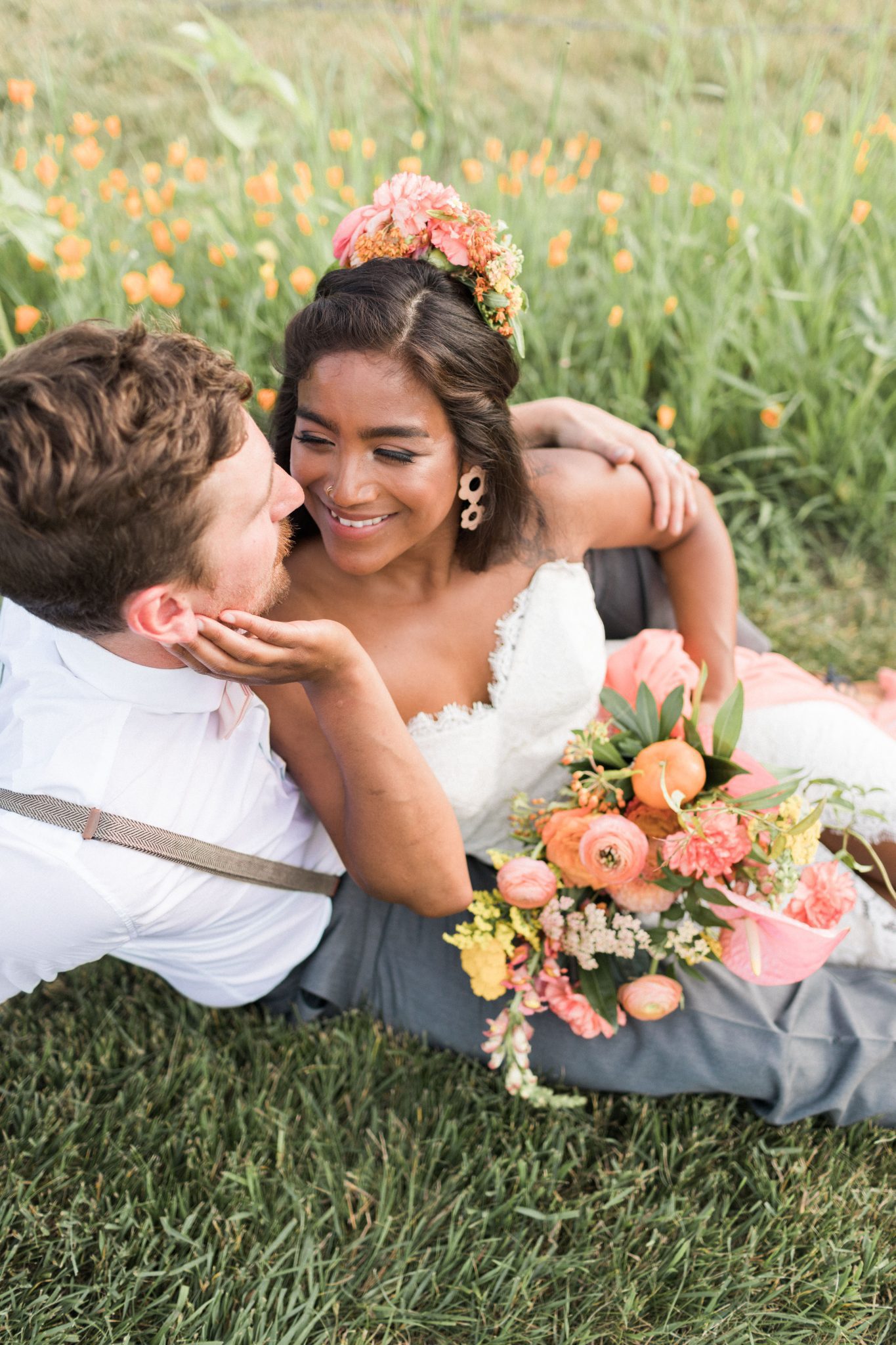 Bride and groom sit in the grass for this countryside wedding with pink and tangerine flowers