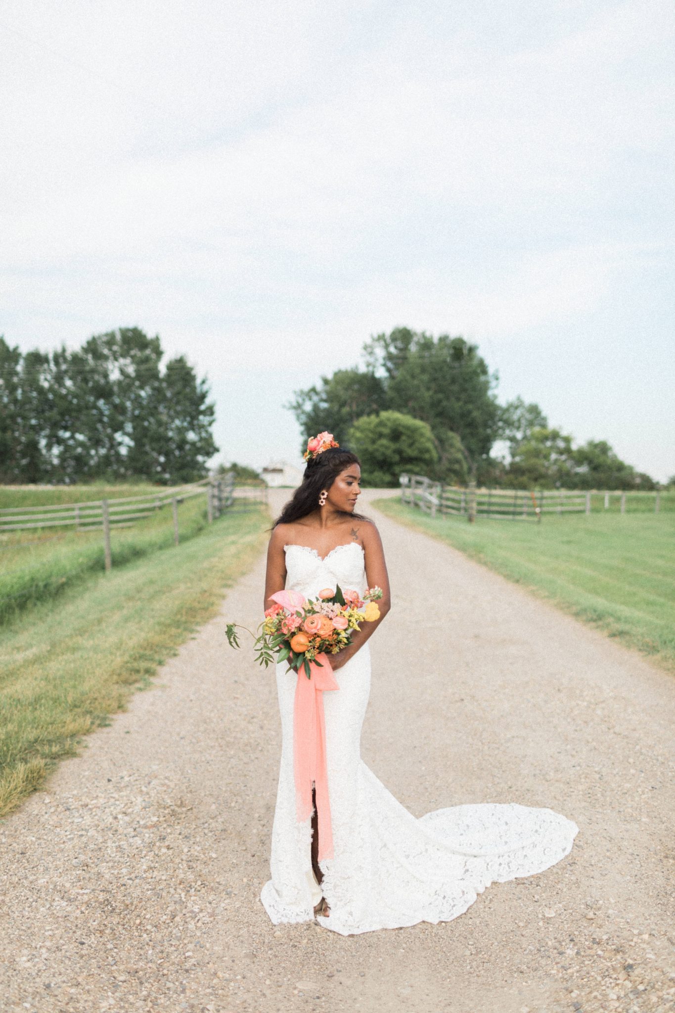 Bride poses on a country road holding a bridal bouquet featuring tangerine and pink florals 