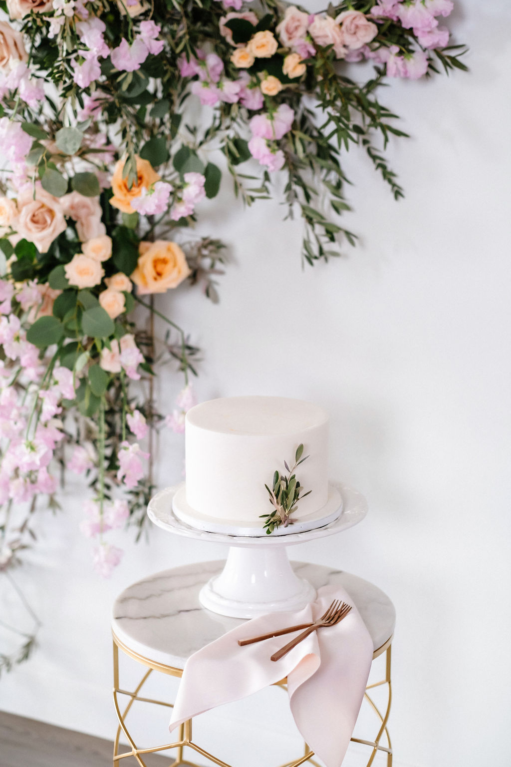One tier simple white wedding cake in front of a floral installation featuring orange and pink roses