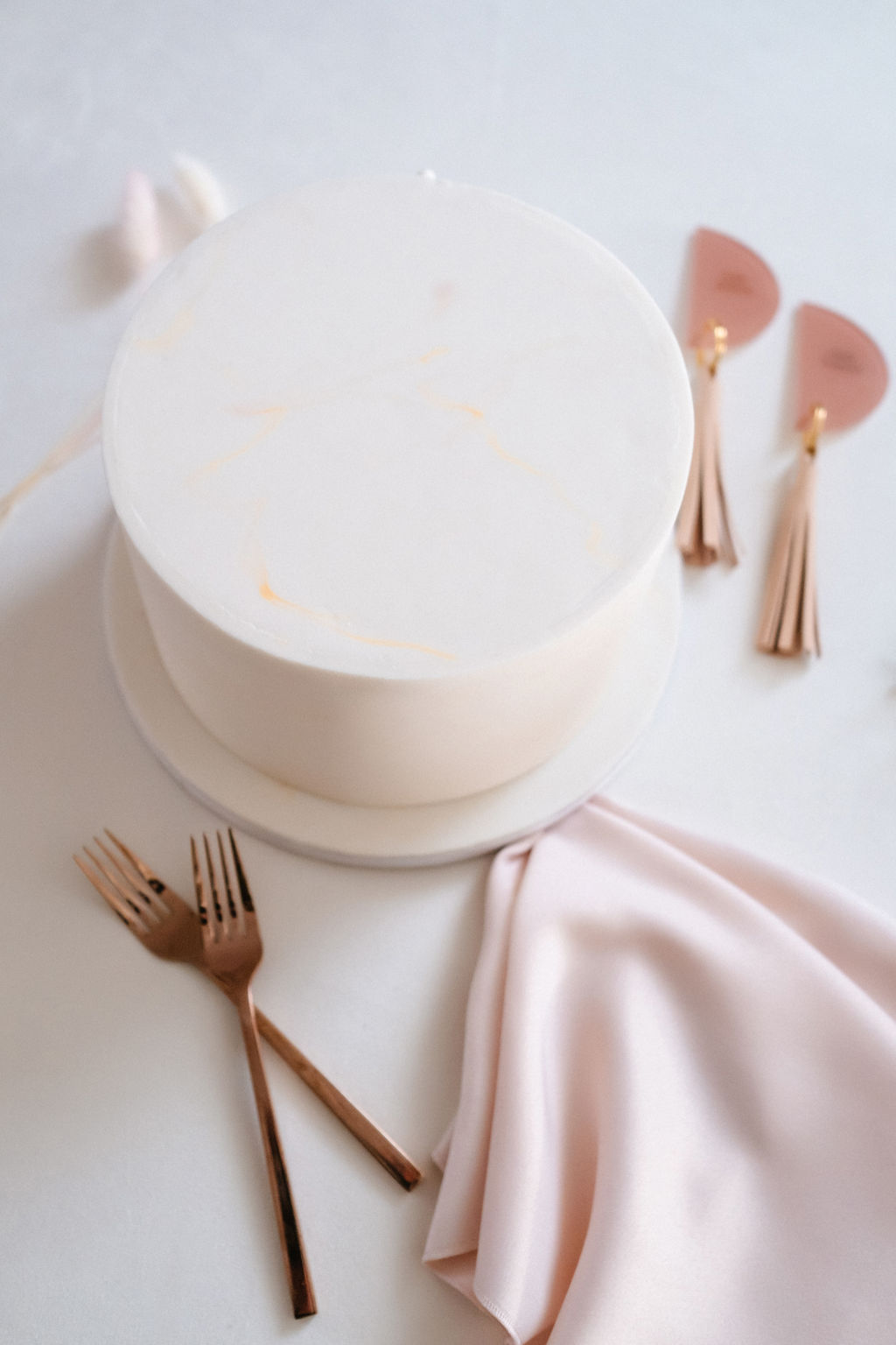 White contemporary wedding cake with flecks of gold styled with a pink satin napkin and rose gold table settings