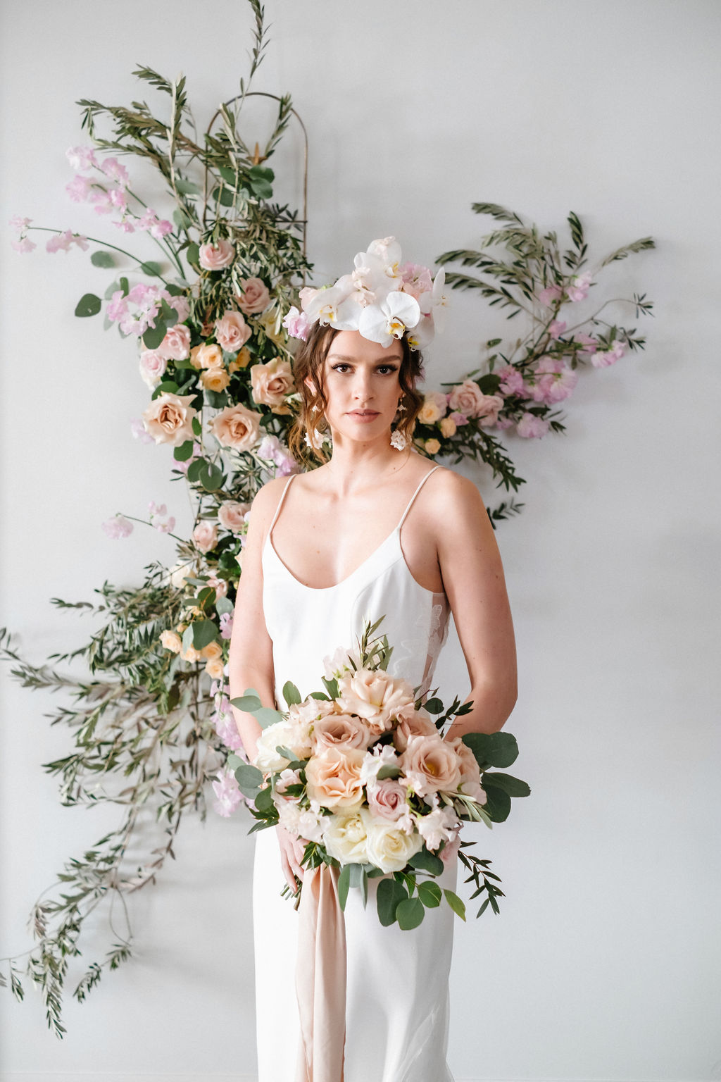 Bride wearing an orchid floral crown in front of a floral installation featuring orange, pink and purple blooms by Creative Edge Flowers 