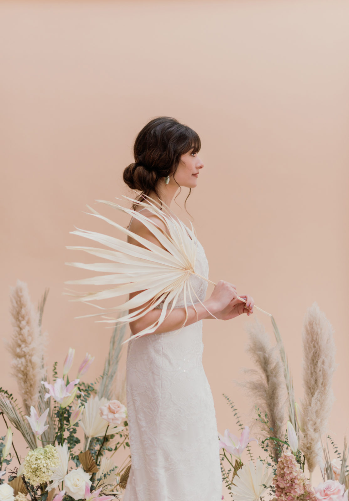 Model holds palm frond and models the Berlin wedding dress from Laudae