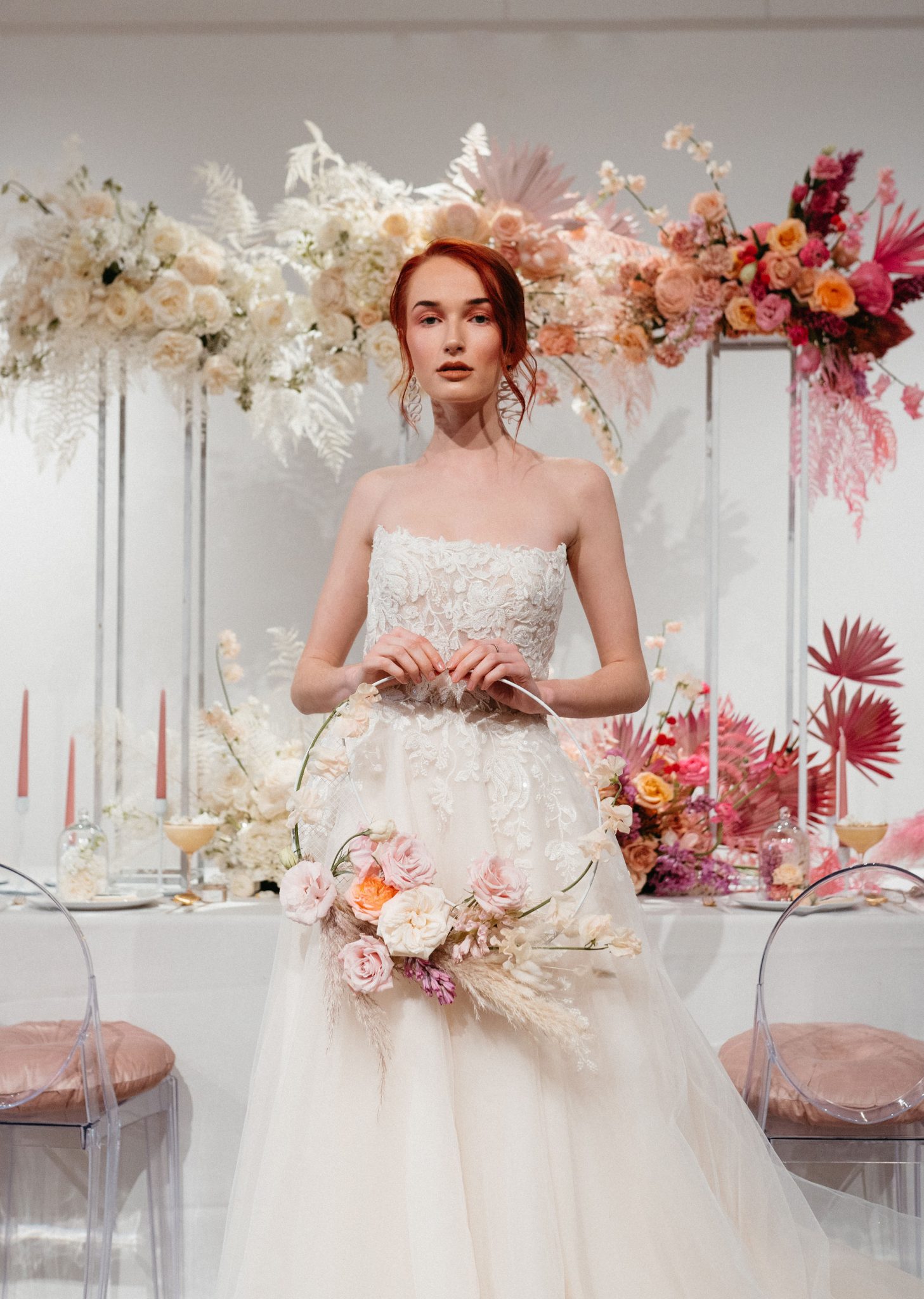 Bride poses in front of an ombre floral installation holding a floral decorated bridal hoop
