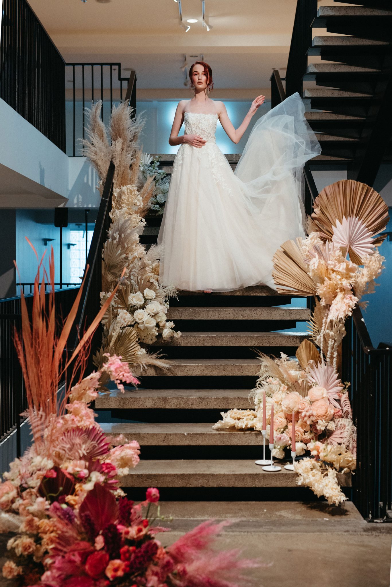 Red head bride poses on a staircase decorated with pink ombre florals at the Pioneer in Calgary Alberta