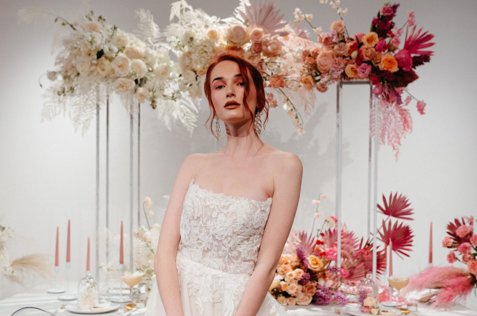 Redhead bride poses in front of a table decorated with a white and pink ombre floral installation