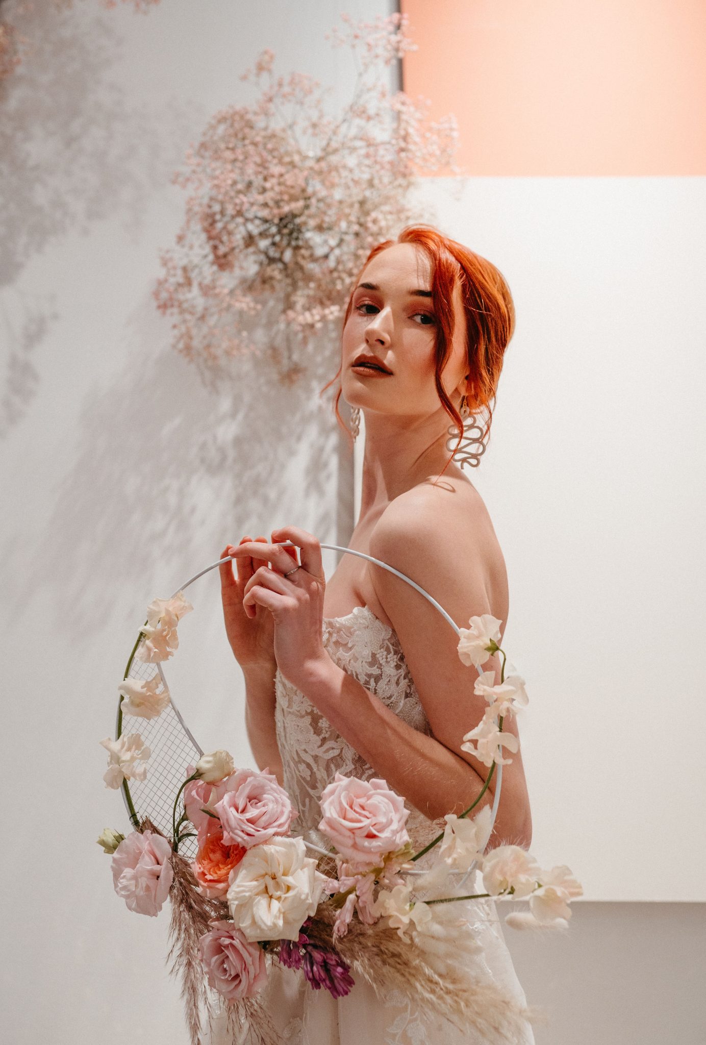 Red head bride poses in front of red, pink and white wedding decor and holds a floral bridal hoop