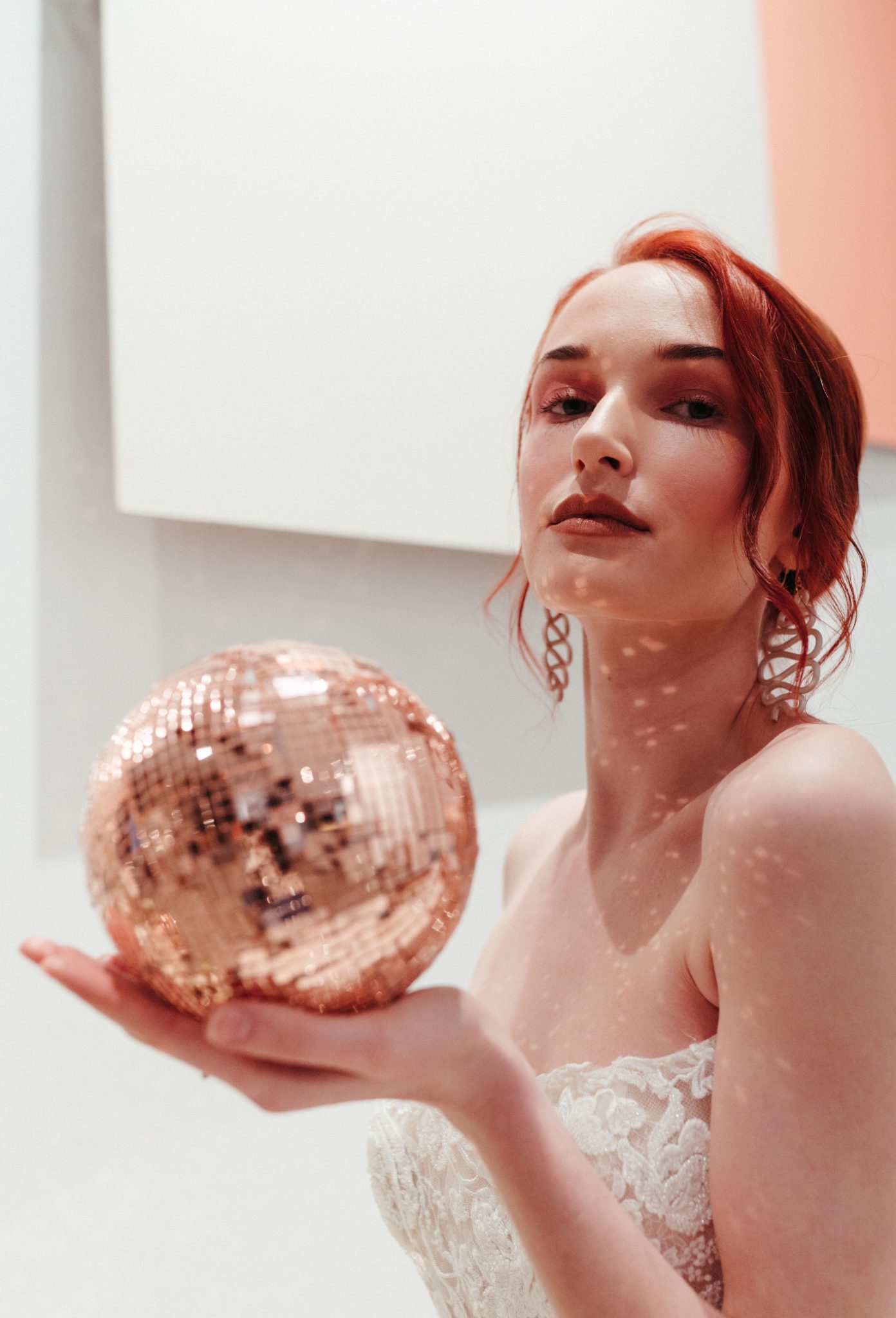Red head bride poses with a rose gold disco ball
