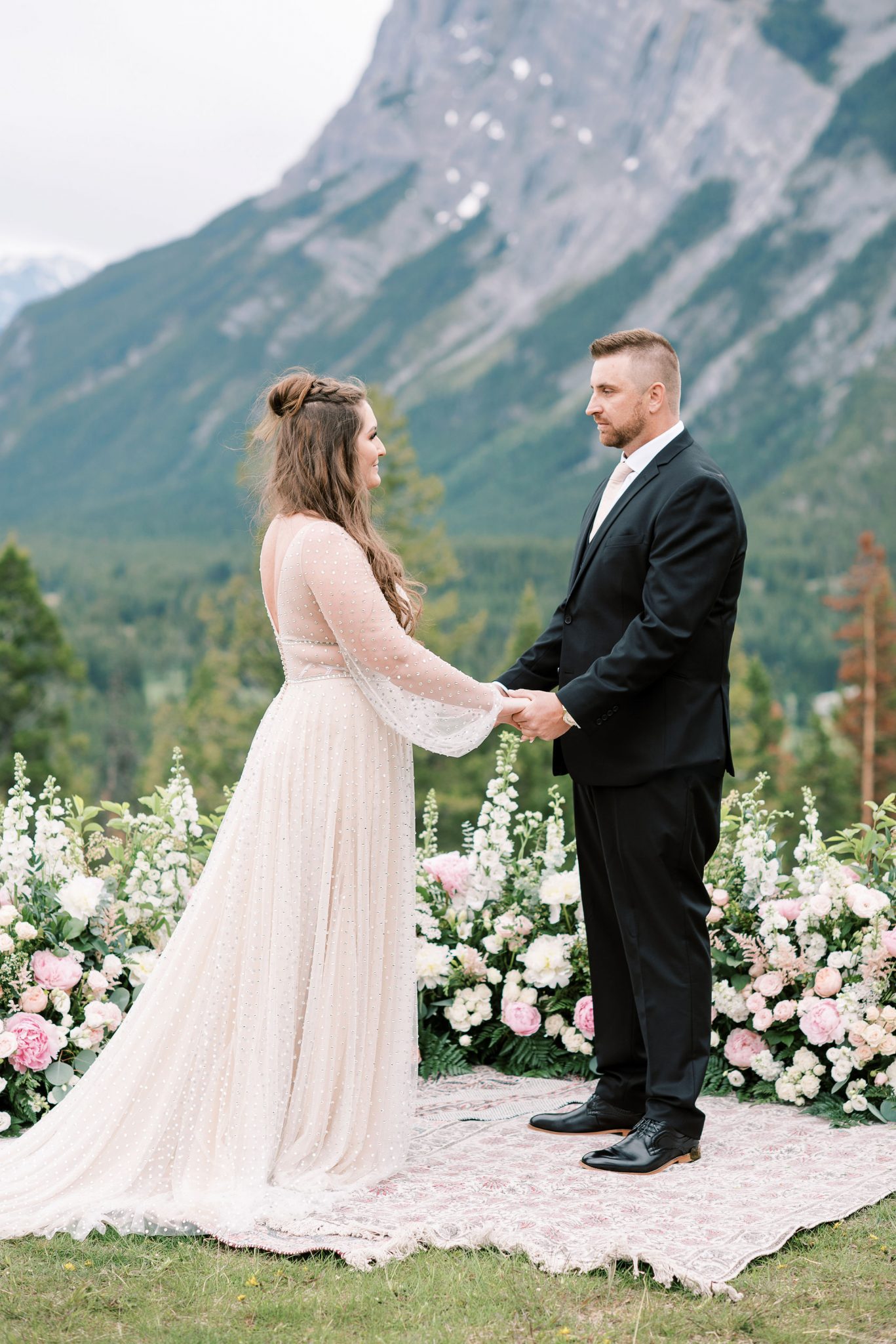 Bride and groom hold hands in front of a grounded floral arch for their mountainside elopement