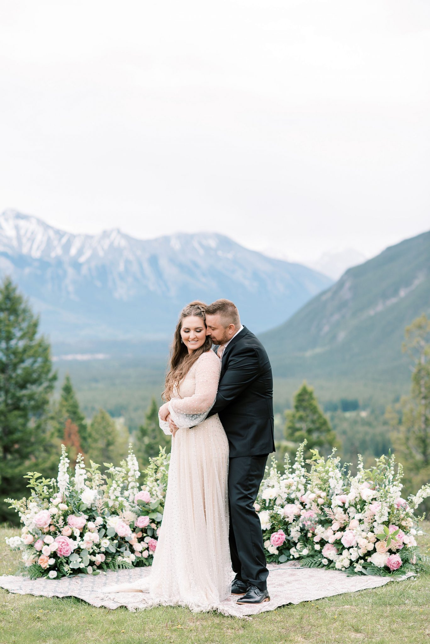 Bride and groom pose in front of a grounded floral arch created by Flowers by Janie for their mountainside elopement
