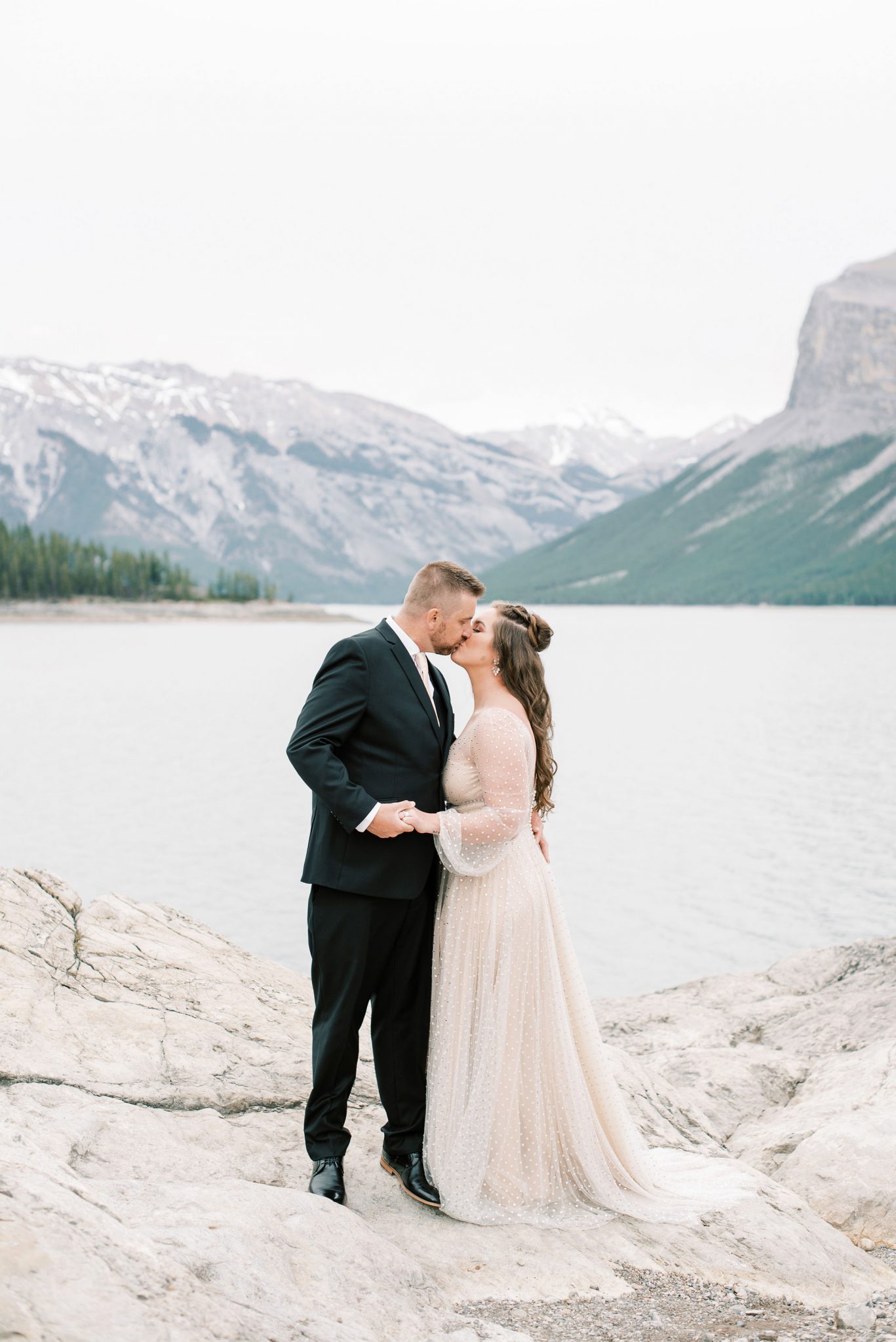 Bride and groom share a kiss on the rocky shore of Lake Minnewanka