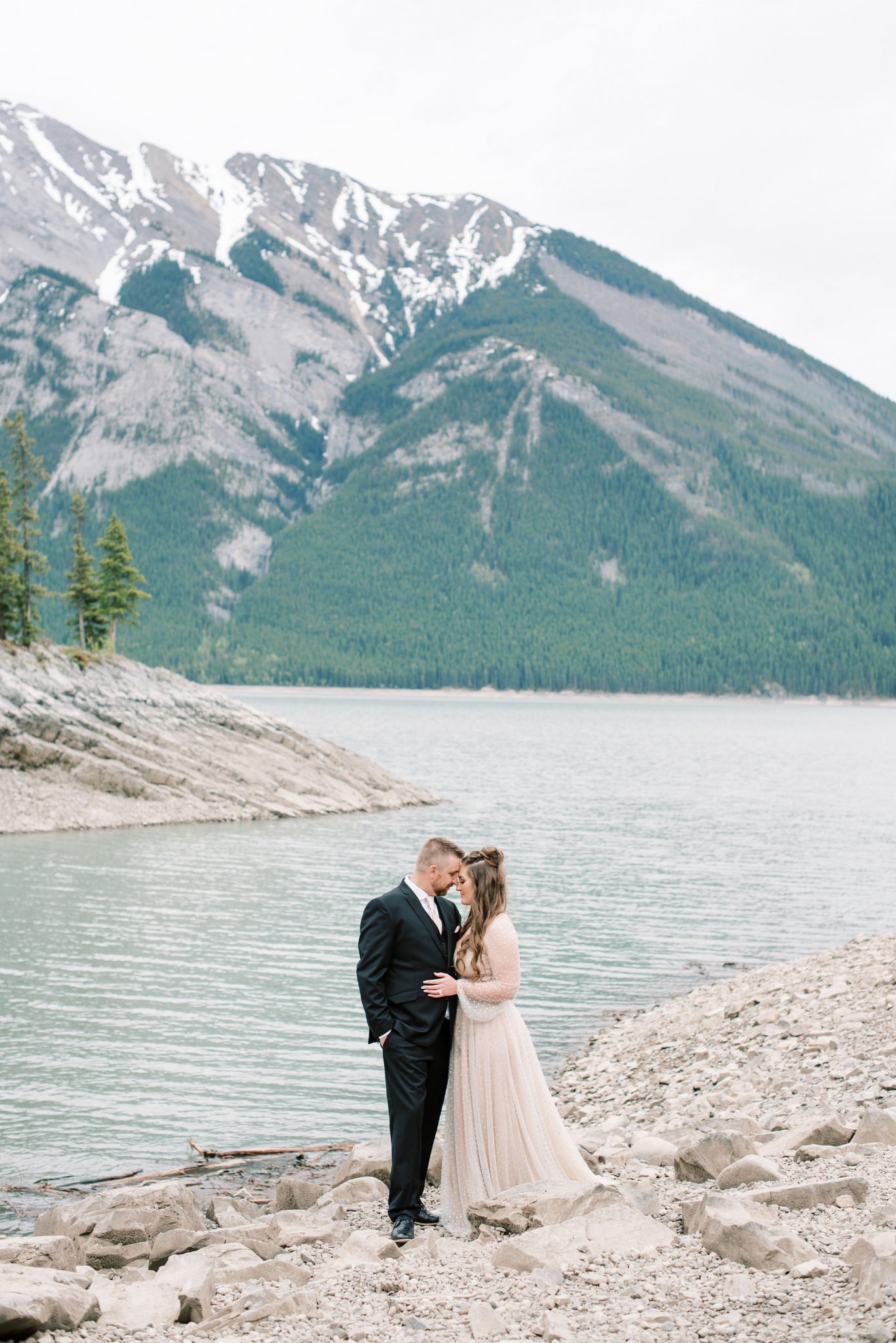 Bride and groom pose on the rocky shore of Lake Minnewanka