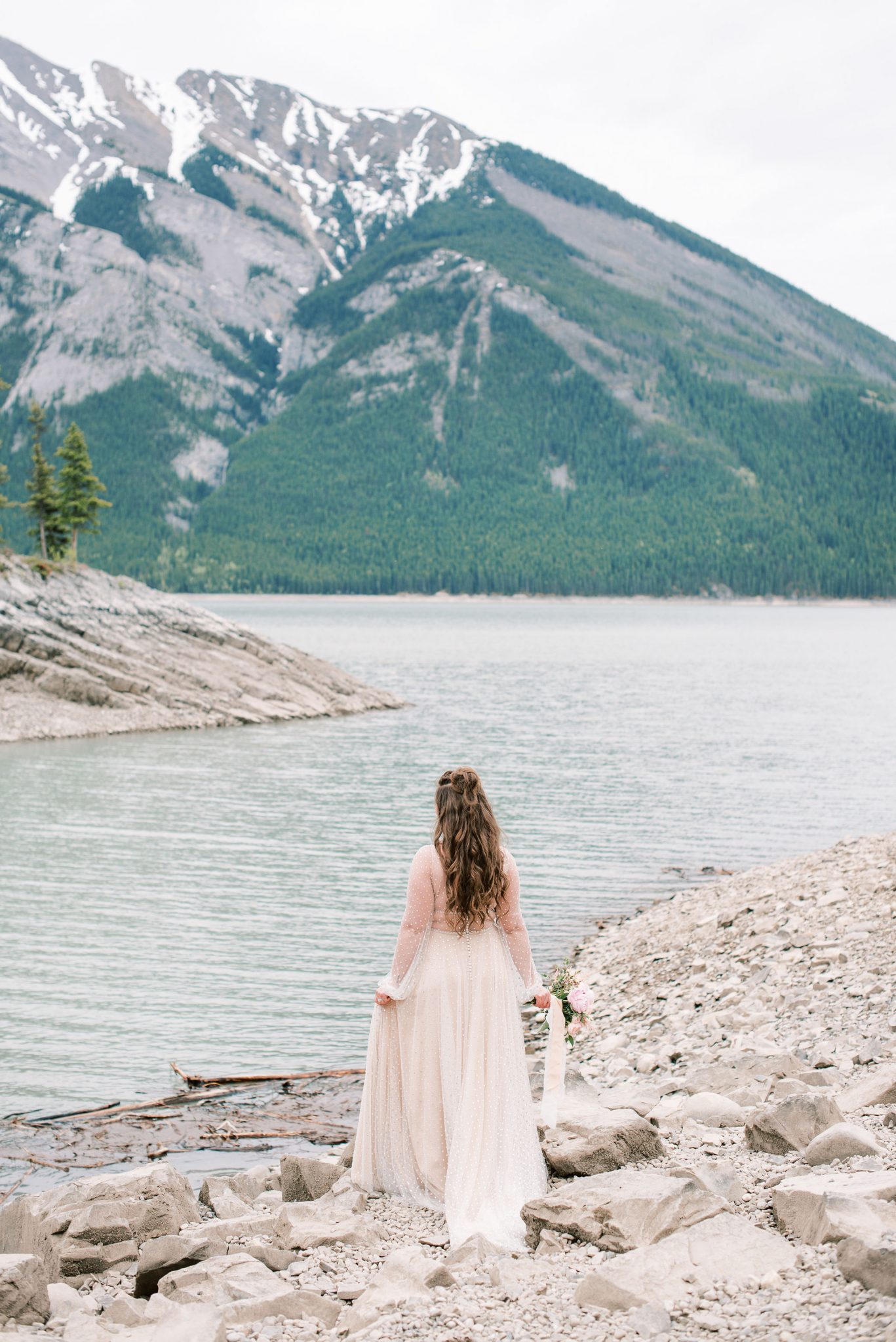 Bride poses along the rocky shore of Lake Minnewanka after eloping in Banff National Park