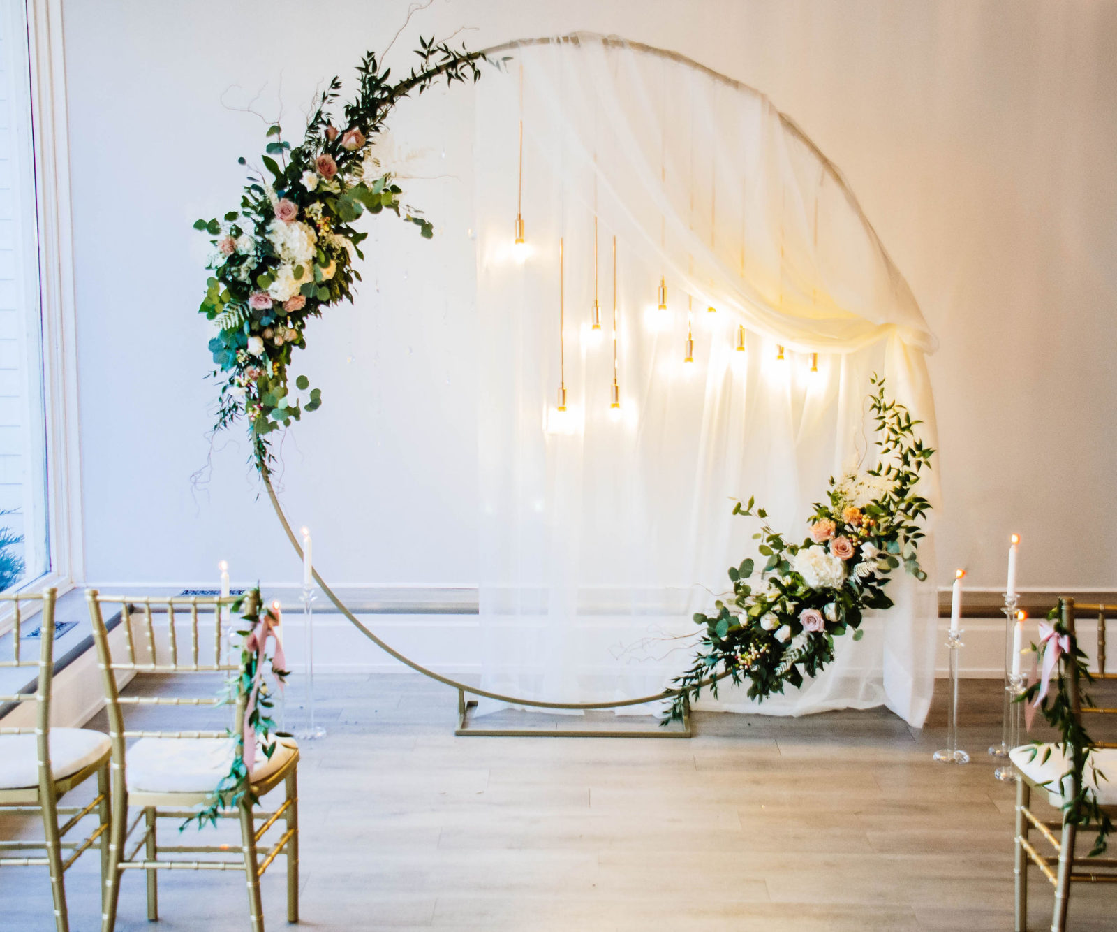 Enchanting ballroom wedding decor inspiration with a circular arch, lush greenery, hanging lights and golden chairs