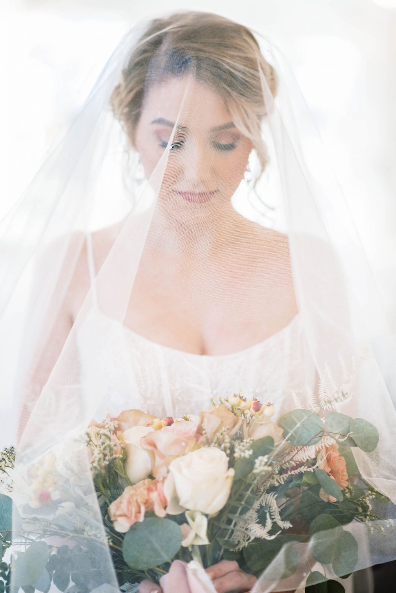 Timeless bridal portrait with the bride's veil over her face and blush bridal bouquet